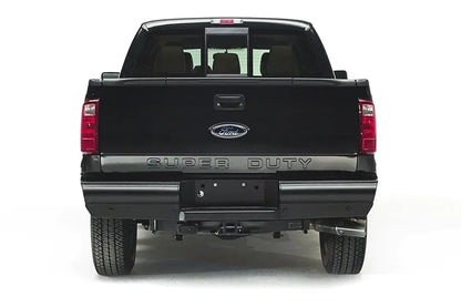 Fab Fours Black Steel Elite rear bumper on a black Ford Super Duty, straight-on rear view, showing the smooth full-width bumper, license plate recess and hitch receiver opening