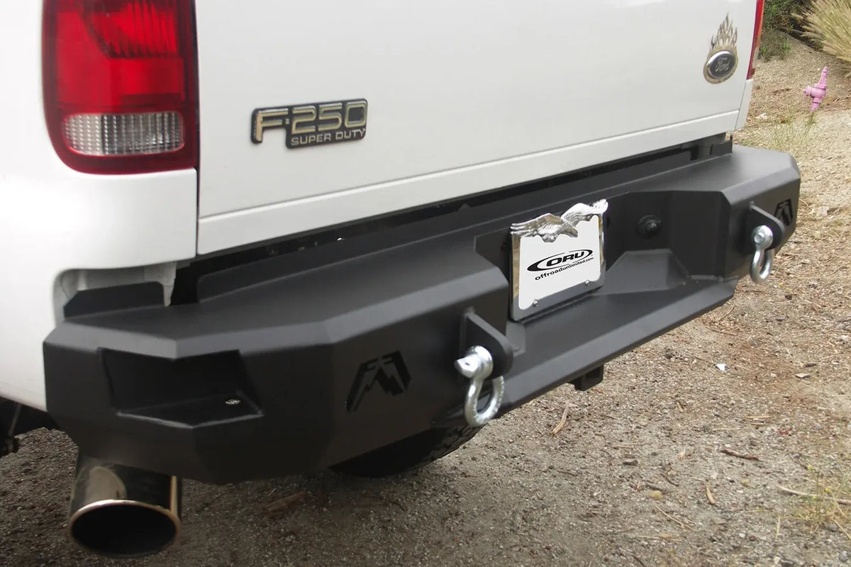 Fab Fours Premium rear bumper on a white Ford F-250 Super Duty outdoors, close-up of the rear passenger corner, showing the angular end cap, Fab Fours logo cutout and D-ring shackle