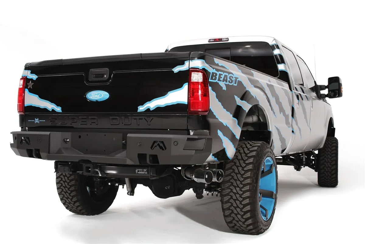 Fab Fours Premium rear bumper on a black and silver Ford Super Duty, rear passenger-side three-quarter view, showing the bumper face, Fab Fours logo cutout and integrated lights