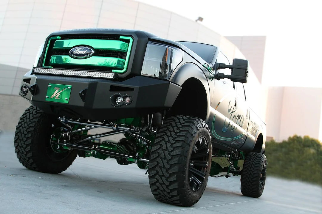 Fab Fours Premium Heavy Duty winch front bumper on a black Ford Super Duty outdoors, front driver-side three-quarter view, showing the bumper face, integrated lights and bumper wing