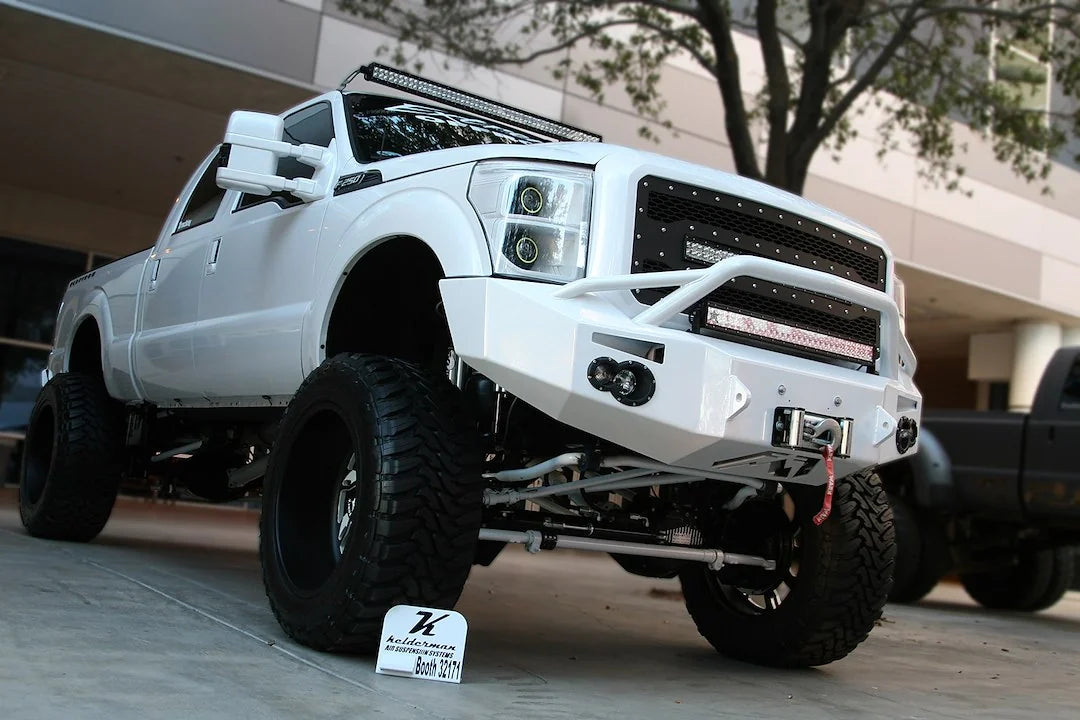 Fab Fours Premium Heavy Duty winch front bumper with pre-runner guard in white on a white Ford Super Duty outdoors, front passenger-side three-quarter view, showing the pre-runner hoop, winch and integrated lights