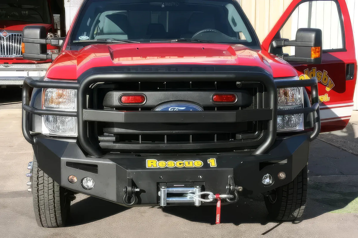 Fab Fours Premium Heavy Duty winch front bumper with full guard on a red Ford Super Duty outdoors, straight-on front view, showing the full grille guard, winch with hook and integrated lights