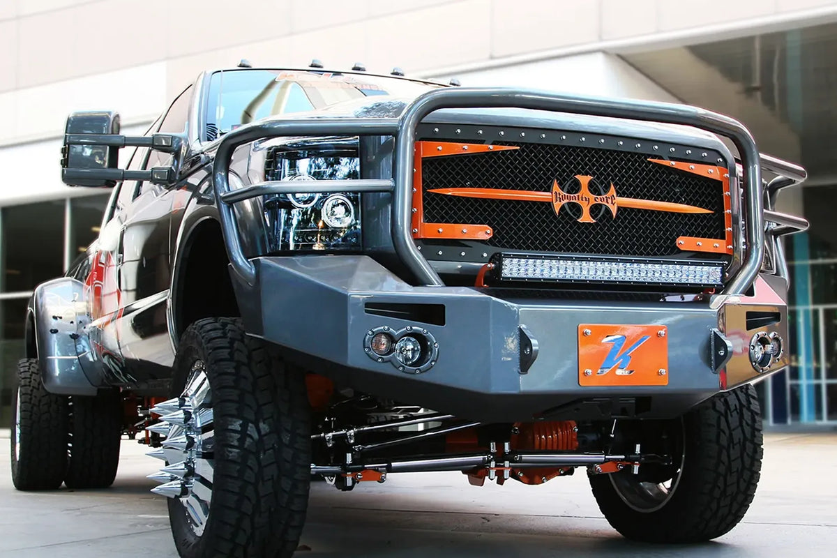 Fab Fours Premium Heavy Duty winch front bumper with full guard on a dark Ford Super Duty dually outdoors, low front view, showing the full tubular grille guard, integrated lights and winch opening