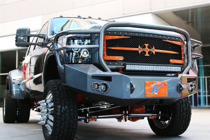 Fab Fours Premium Heavy Duty winch front bumper with full guard on a dark Ford Super Duty dually outdoors, low front view, showing the full tubular grille guard, integrated lights and winch opening