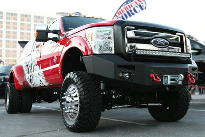 Fab Fours Premium Heavy Duty winch front bumper on a red and white Ford Super Duty dually outdoors, front passenger-side three-quarter view, showing the winch, D-ring shackles and integrated lights