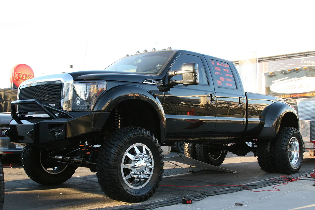 Fab Fours Premium Heavy Duty winch front bumper with pre-runner guard on a black Ford Super Duty dually outdoors, front driver-side three-quarter view, showing the tubular pre-runner hoop, integrated lights and bumper wing