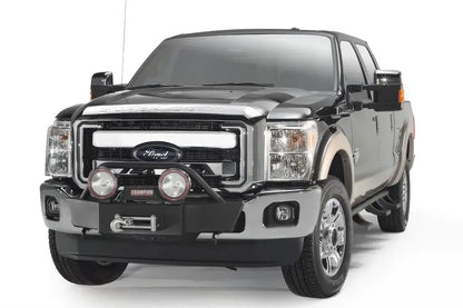 Fab Fours winch mount on a black and tan Ford Super Duty, front three-quarter view, showing the winch, light hoop and round off-road lights