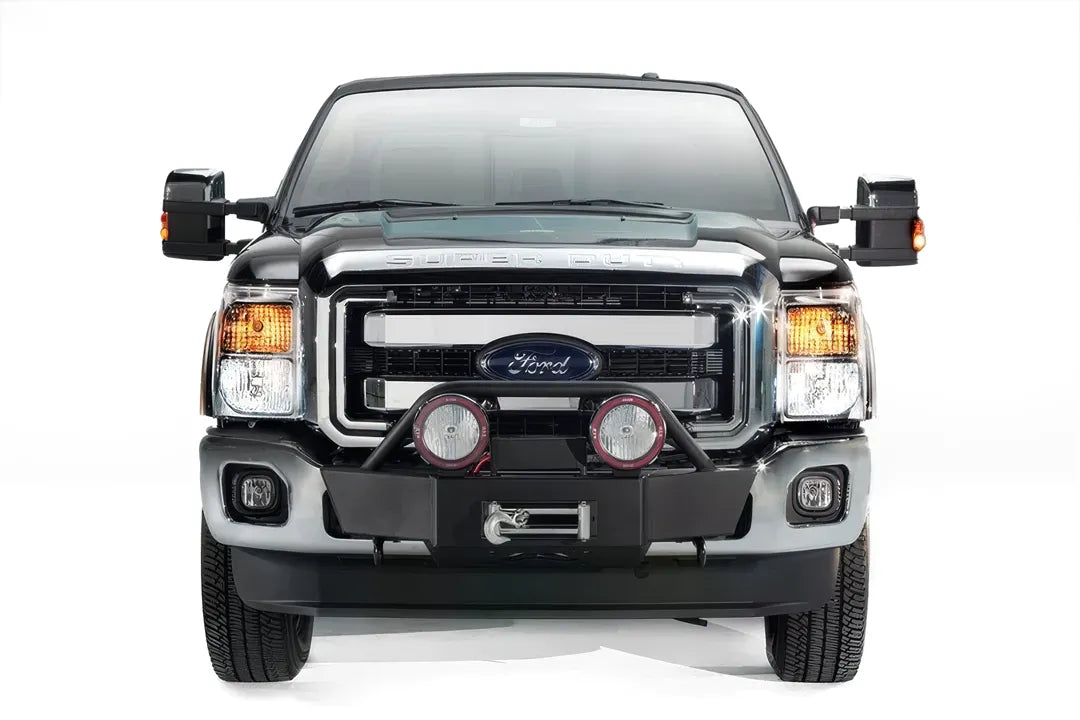 Fab Fours winch mount on a black and tan Ford Super Duty, straight-on front view, showing the hidden winch cradle, light hoop and pair of round off-road lights