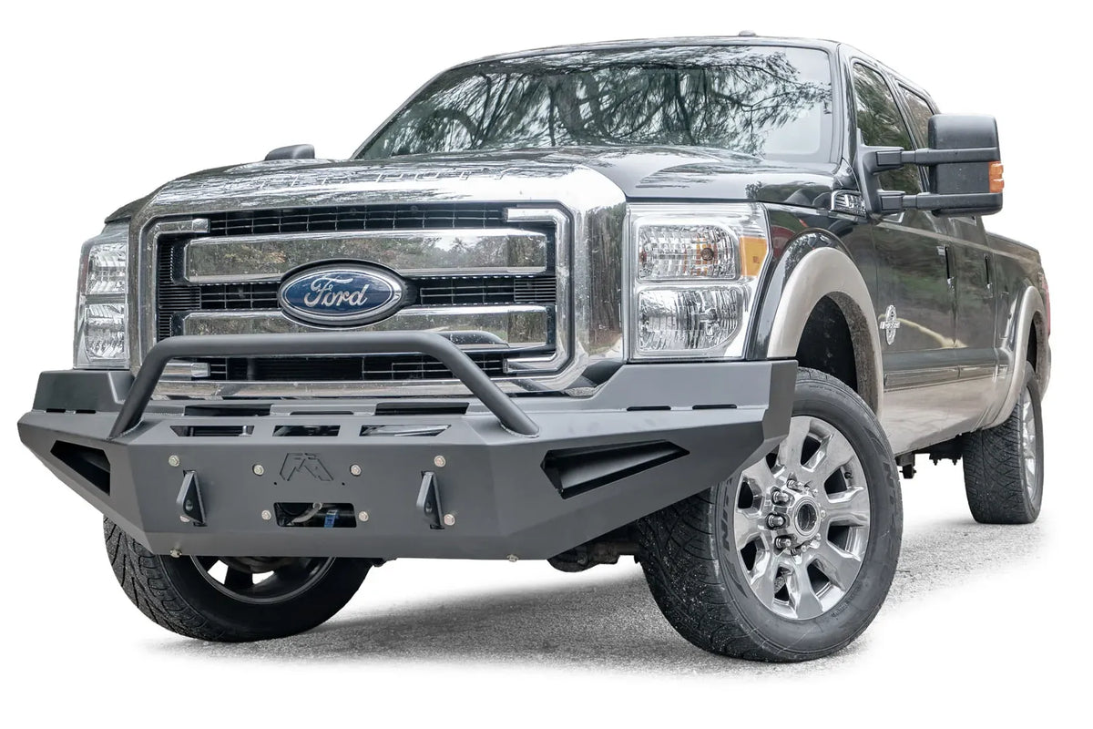 Fab Fours Red Steel front bumper with pre-runner guard on a dark green and tan Ford Super Duty, front driver-side three-quarter view, showing the pre-runner hoop, winch plate and shackle tabs