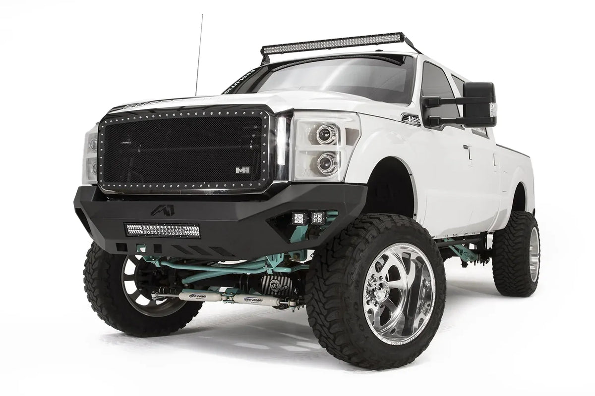 Fab Fours Vengeance front bumper on a white Ford Super Duty, front driver-side three-quarter view, showing the center light bar, Fab Fours logo cutout and pod light pockets
