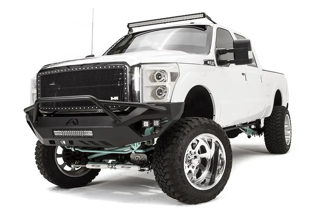 Fab Fours Vengeance front bumper with pre-runner guard on a white Ford Super Duty, front driver-side three-quarter view, showing the tubular pre-runner hoop, center light bar and pod lights