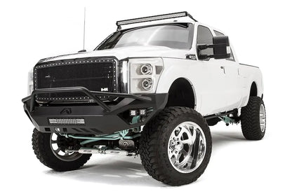 Fab Fours Vengeance front bumper with pre-runner guard on a white Ford Super Duty, front driver-side three-quarter view, showing the tubular pre-runner hoop, center light bar and pod lights