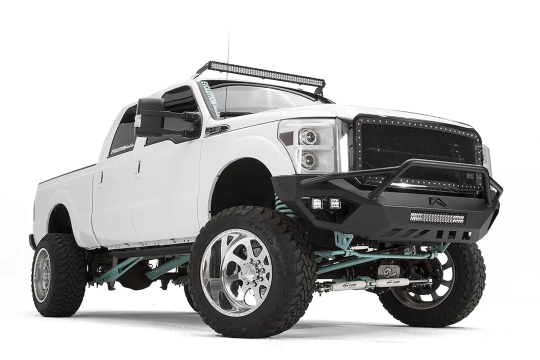 Fab Fours Vengeance front bumper with pre-runner guard on a white Ford Super Duty, front passenger-side three-quarter view, showing the pre-runner hoop, center light bar and pod lights