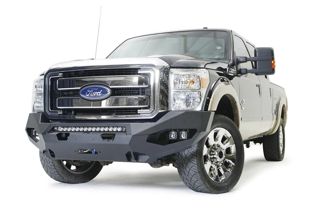 Fab Fours Matrix front winch bumper on a black and tan Ford Super Duty, front driver-side three-quarter view, showing the center light bar, pod lights and winch opening