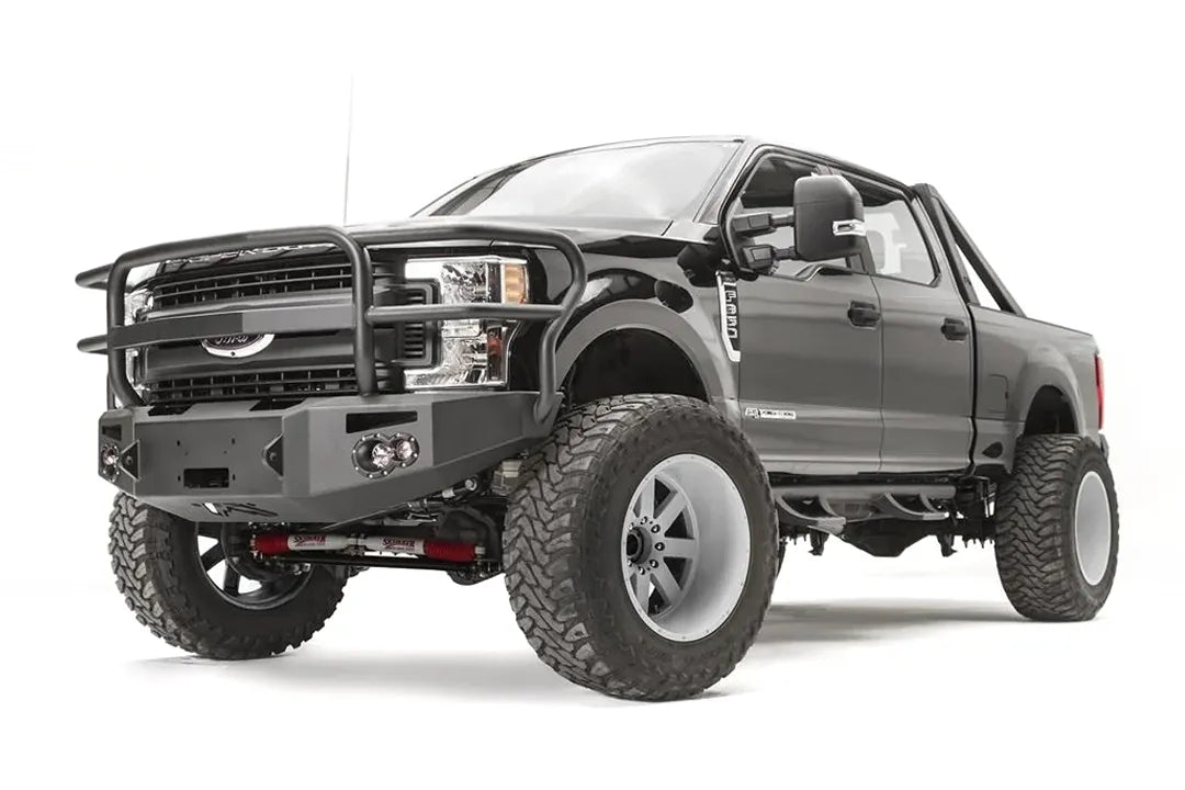 Fab Fours Premium winch front bumper with full guard on a black Ford Super Duty, front driver-side three-quarter view, showing the full tubular grille guard, winch opening and integrated lights