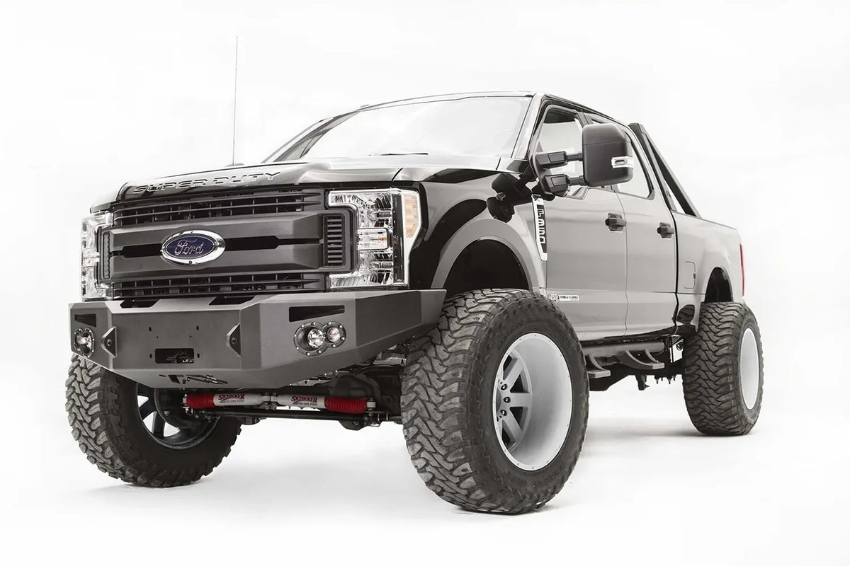 Fab Fours Premium winch front bumper on a black Ford Super Duty, front driver-side three-quarter view, showing the winch opening, integrated lights and bumper end cap