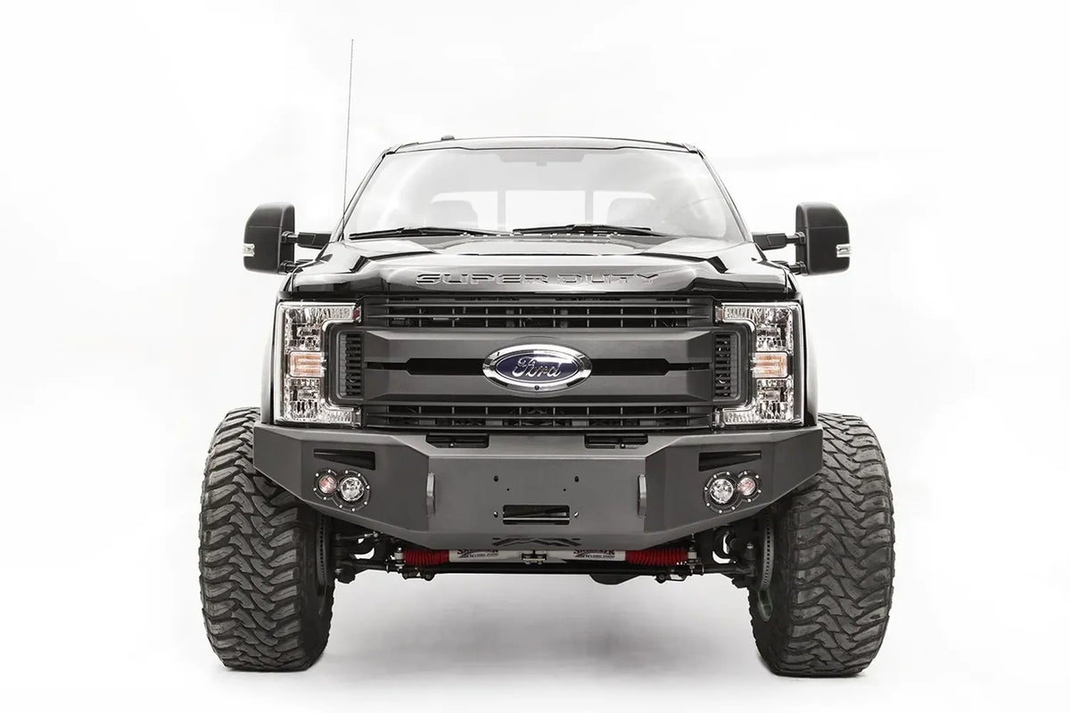 Fab Fours Premium winch front bumper on a black Ford Super Duty, straight-on front view, showing the winch opening, pair of integrated lights and wraparound wings