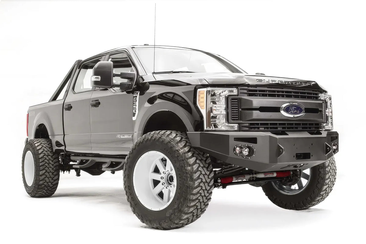 Fab Fours Premium winch front bumper on a black Ford Super Duty, front passenger-side three-quarter view, showing the winch opening, integrated lights and bumper wing