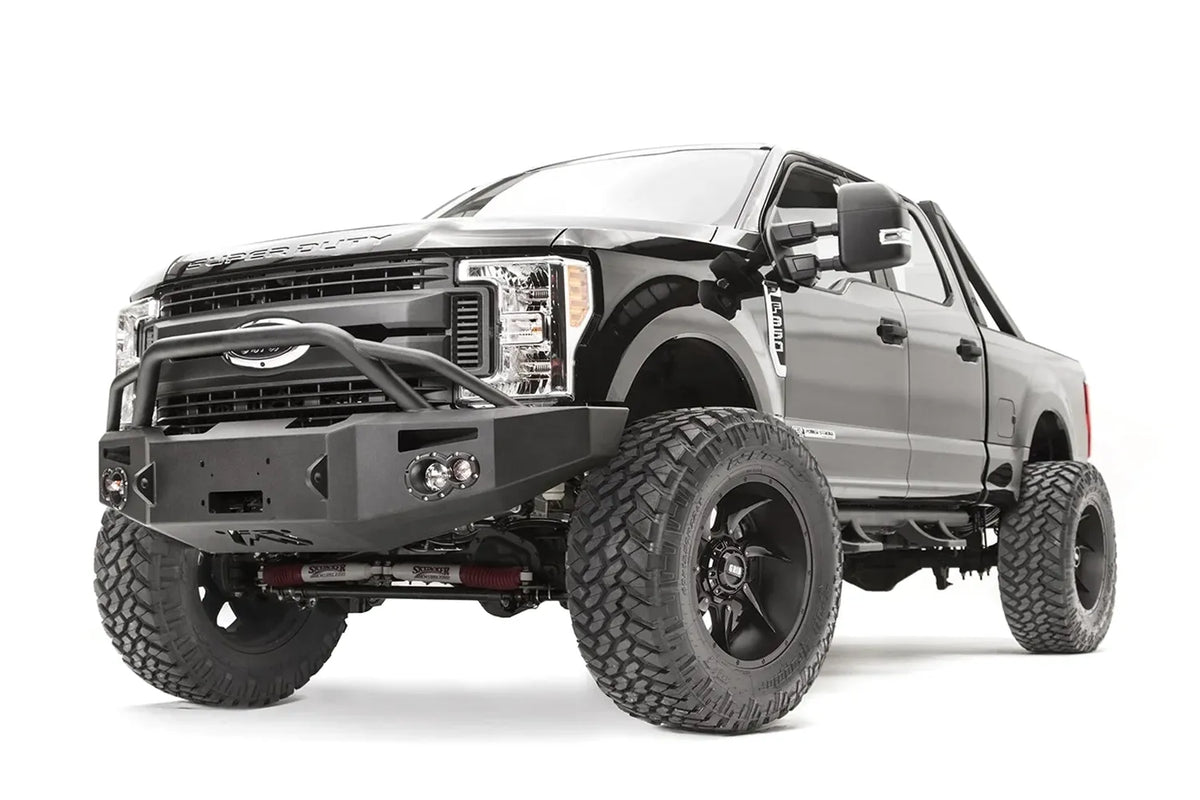 Fab Fours Premium winch front bumper with pre-runner guard on a black Ford Super Duty, front driver-side three-quarter view, showing the tubular pre-runner hoop, winch opening and integrated lights