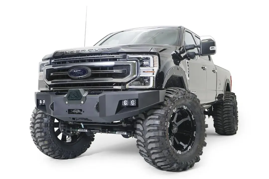 Fab Fours Premium Winch front bumper on a black Ford Super Duty, front driver-side three-quarter view, showing the center winch opening, flush-mounted LED light pods, and angular steel end caps