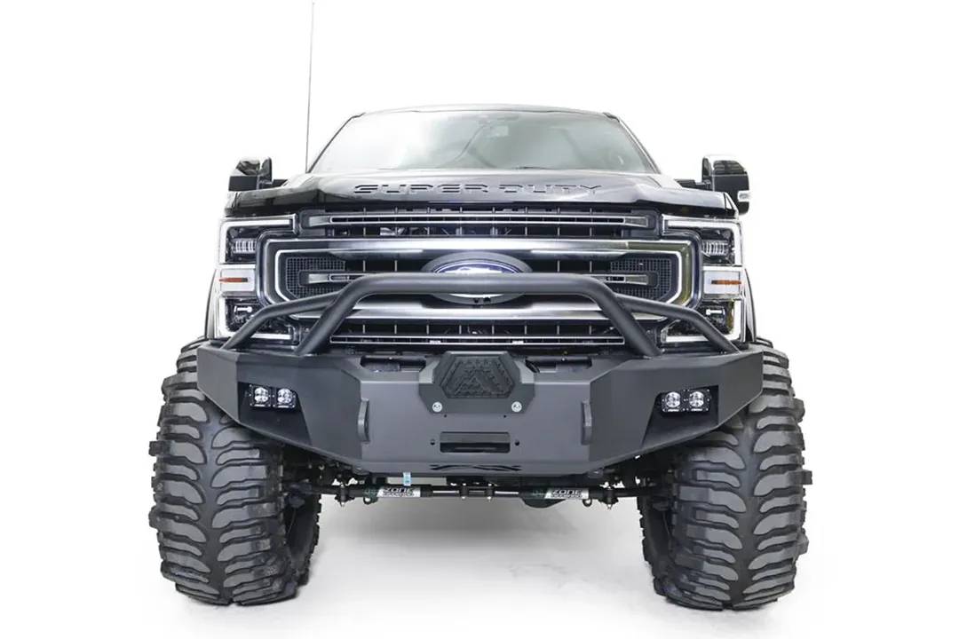 Fab Fours Premium Winch front bumper with pre-runner guard on a black Ford Super Duty, straight-on front view, showing the tubular pre-runner hoop, the center winch opening, flush-mounted LED light pods, and angular steel end caps