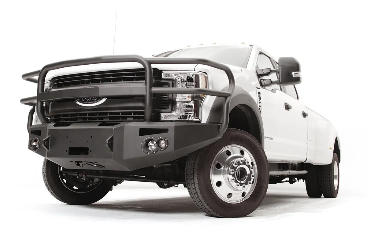 Fab Fours Premium Winch front bumper with full guard on a white Ford Super Duty F-450/F-550, front driver-side three-quarter view, showing full grille guard hoops, the center winch opening, round light cutouts, and angular steel end caps
