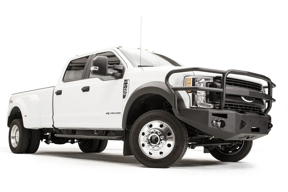 Fab Fours Premium Winch front bumper with full guard on a white Ford Super Duty F-450/F-550, front passenger-side three-quarter view, showing full grille guard hoops, the center winch opening, round light cutouts, and angular steel end caps