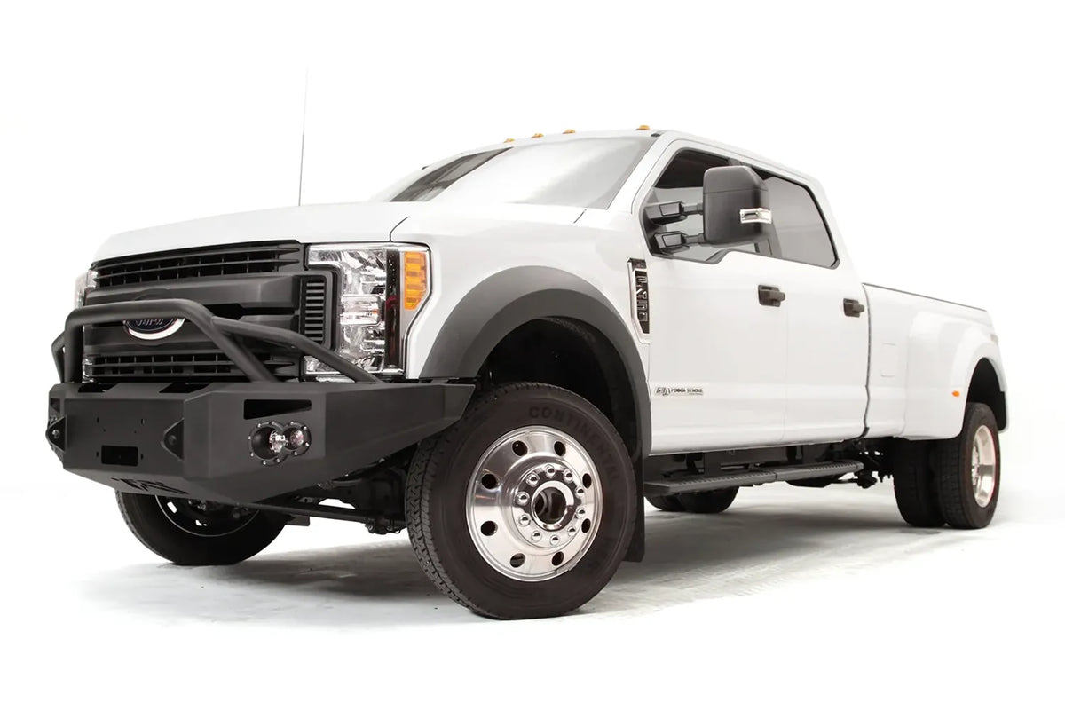 Fab Fours Premium Winch front bumper with pre-runner guard on a white Ford Super Duty F-450/F-550, front driver-side three-quarter view, showing the tubular pre-runner hoop, the center winch opening, round light cutouts, and angular steel end caps