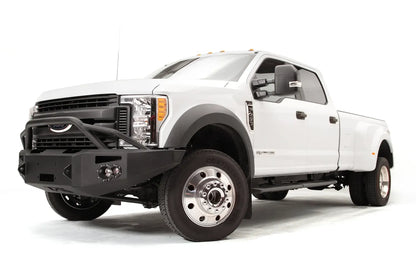 Fab Fours Premium Winch front bumper with pre-runner guard on a white Ford Super Duty F-450/F-550, front driver-side three-quarter view, showing the tubular pre-runner hoop, the center winch opening, round light cutouts, and angular steel end caps