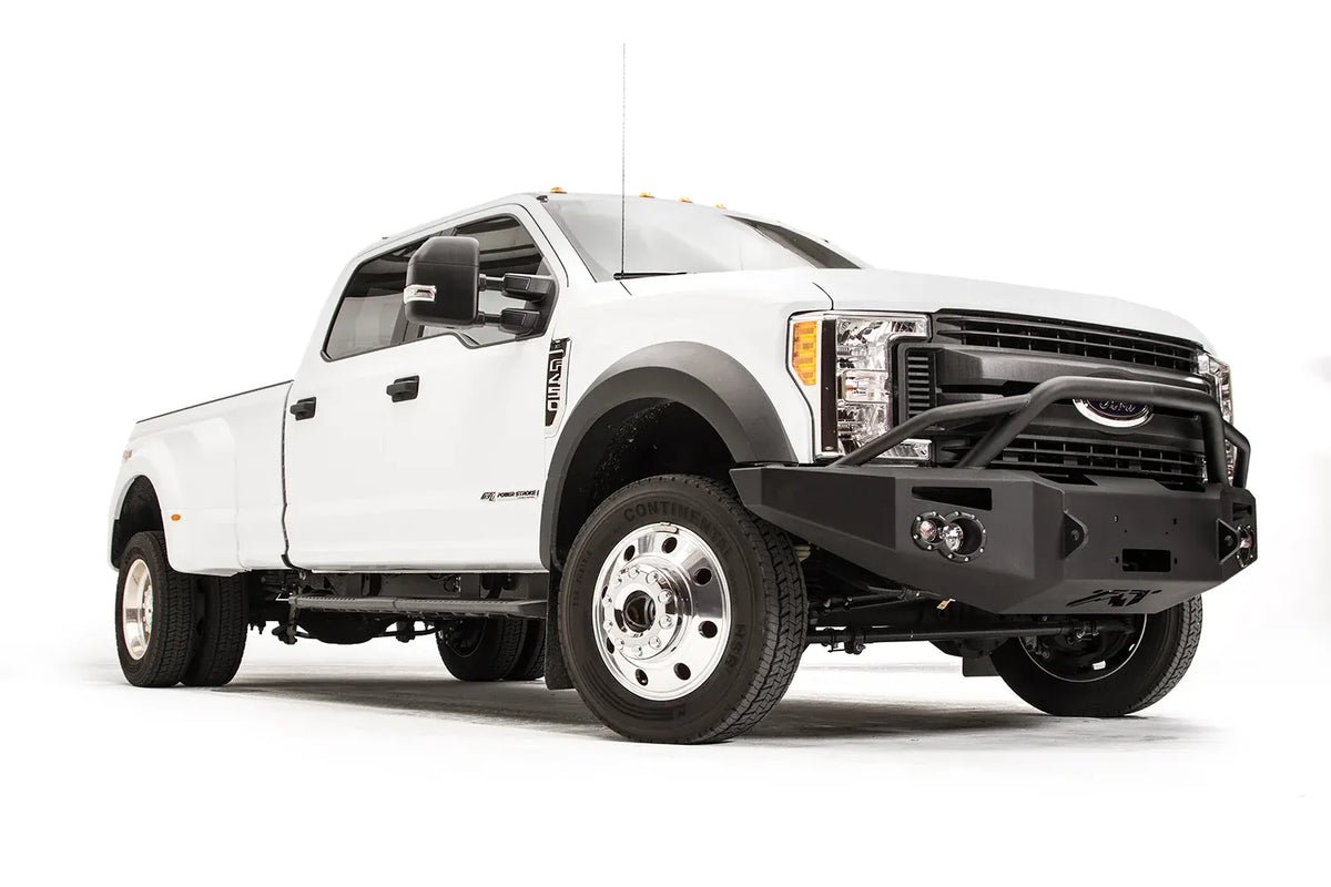 Fab Fours Premium Winch front bumper with pre-runner guard on a white Ford Super Duty F-450/F-550, front passenger-side three-quarter view, showing the tubular pre-runner hoop, the center winch opening, round light cutouts, and angular steel end caps