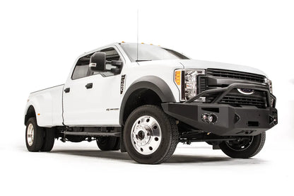 Fab Fours Premium Winch front bumper with pre-runner guard on a white Ford Super Duty F-450/F-550, front passenger-side three-quarter view, showing the tubular pre-runner hoop, the center winch opening, round light cutouts, and angular steel end caps