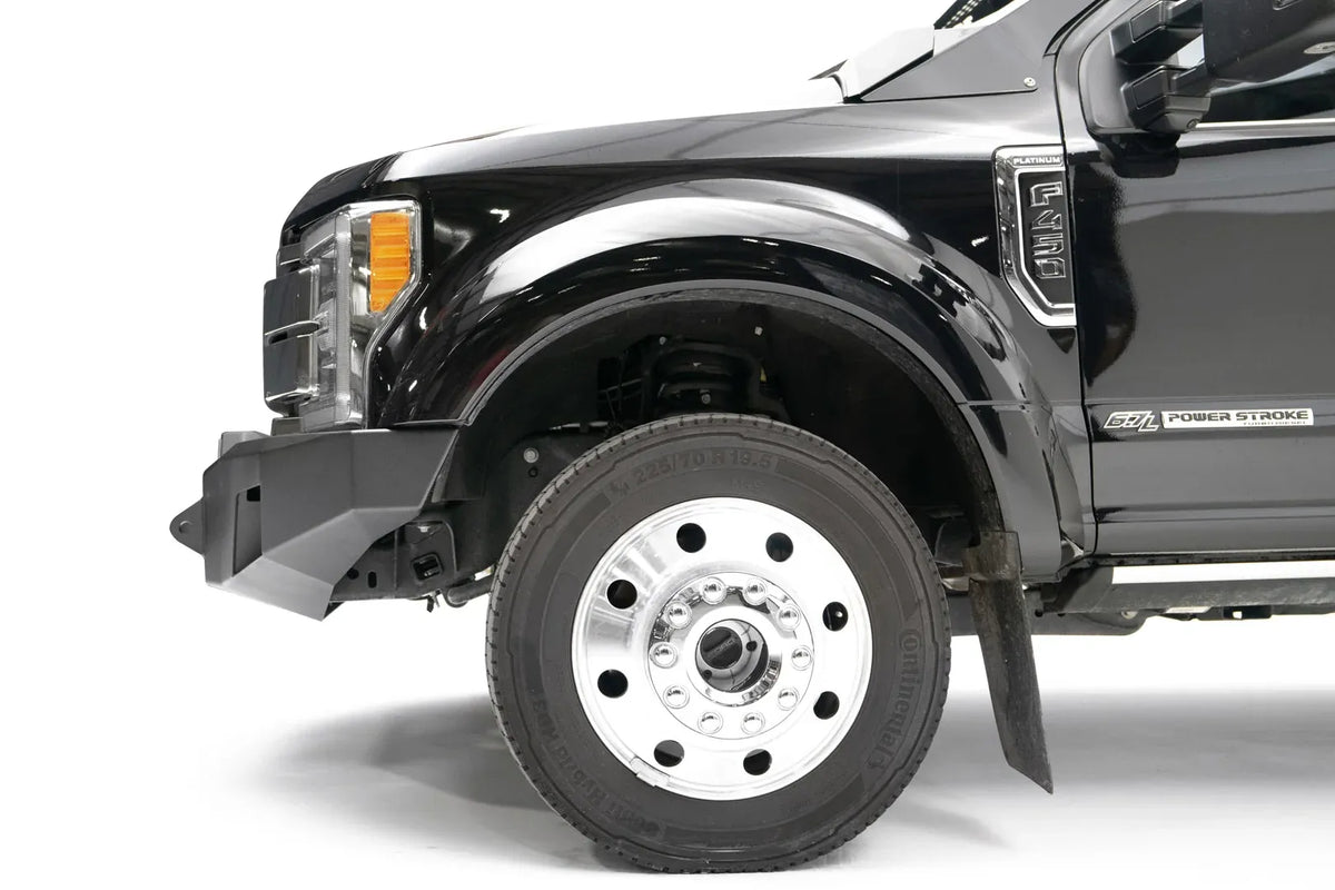 Fab Fours Premium Winch front bumper on a black Ford Super Duty XL F-450/F-550, driver-side profile view of the front corner, showing the center winch opening, angular steel end caps, and integrated tow points