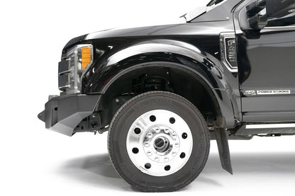 Fab Fours Premium Winch front bumper on a black Ford Super Duty XL F-450/F-550, driver-side profile view of the front corner, showing the center winch opening, angular steel end caps, and integrated tow points