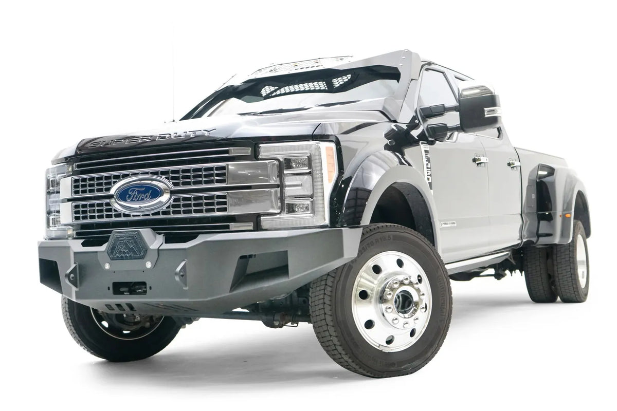 Fab Fours Premium Winch front bumper on a black Ford Super Duty XL F-450/F-550, front driver-side three-quarter view, showing the center winch opening, angular steel end caps, and integrated tow points