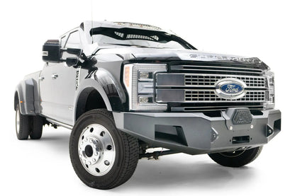 Fab Fours Premium Winch front bumper on a black Ford Super Duty XL F-450/F-550, front passenger-side three-quarter view, showing the center winch opening, angular steel end caps, and integrated tow points