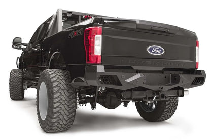 Fab Fours Vengeance rear bumper on a black Ford Super Duty, rear driver-side three-quarter view, showing honeycomb-pattern side cutouts, the center license plate recess, and angular steel wings