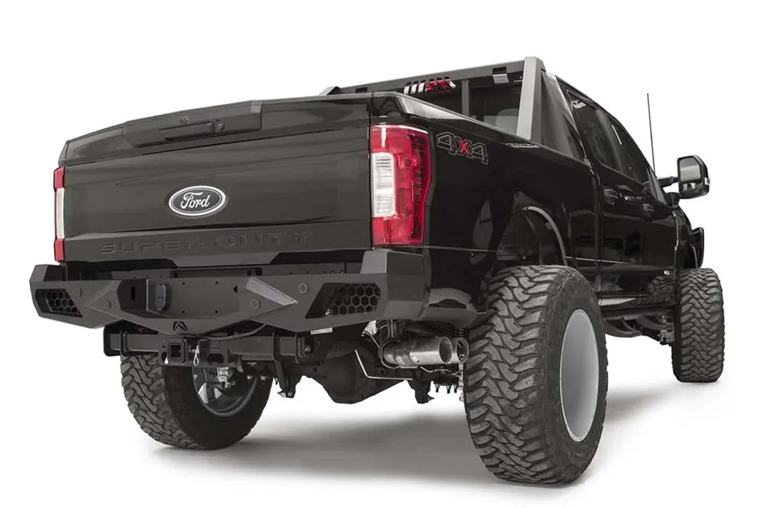 Fab Fours Vengeance rear bumper on a black Ford Super Duty, rear passenger-side three-quarter view, showing honeycomb-pattern side cutouts, the center license plate recess, and angular steel wings