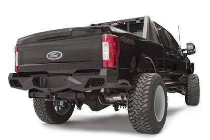 Fab Fours Vengeance rear bumper on a black Ford Super Duty, rear passenger-side three-quarter view, showing honeycomb-pattern side cutouts, the center license plate recess, and angular steel wings