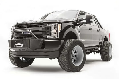 Fab Fours winch mount with pre-runner hoop on a black Ford Super Duty, front driver-side three-quarter view, showing the winch mount plate with fairlead, the tubular pre-runner hoop, and the factory bumper integration