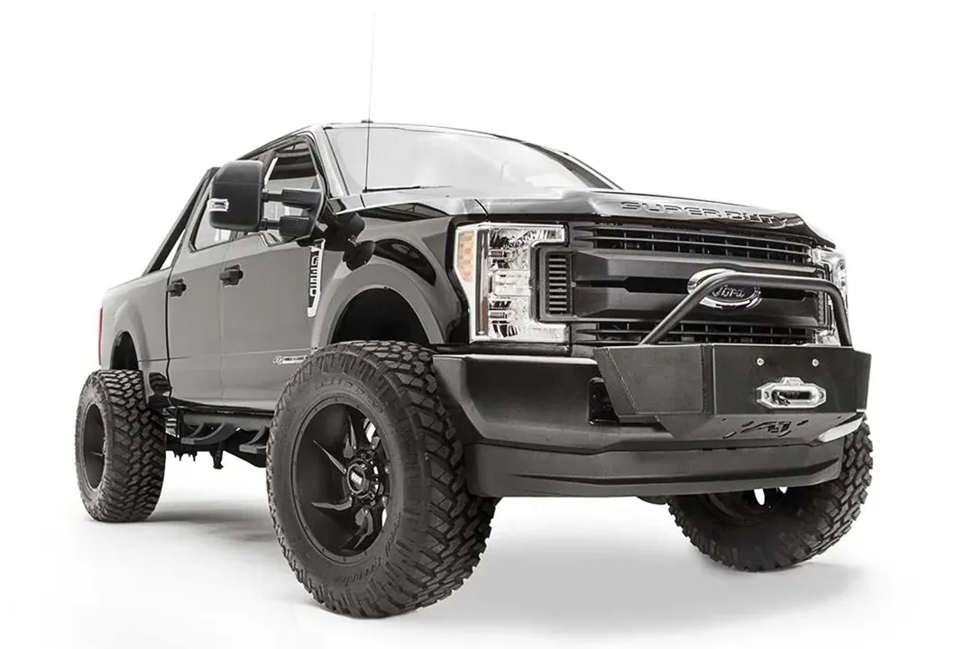 Fab Fours winch mount with pre-runner hoop on a black Ford Super Duty, front passenger-side three-quarter view, showing the winch mount plate with fairlead, the tubular pre-runner hoop, and the factory bumper integration