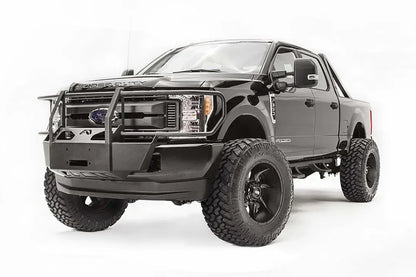 Fab Fours winch mount with full guard on a black Ford Super Duty, front driver-side three-quarter view, showing full grille guard uprights, the winch mount plate, and the factory bumper integration