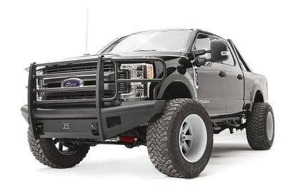Fab Fours Black Steel Elite front bumper with full guard on a black Ford Super Duty, front driver-side three-quarter view, showing full grille guard uprights and side hoops, the smooth steel face, mesh-backed side openings, and the center license plate mount