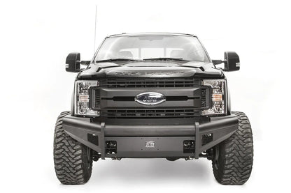 Fab Fours Black Steel Elite front bumper on a black Ford Super Duty, straight-on front view, showing the smooth steel face, mesh-backed side openings, and the center license plate mount