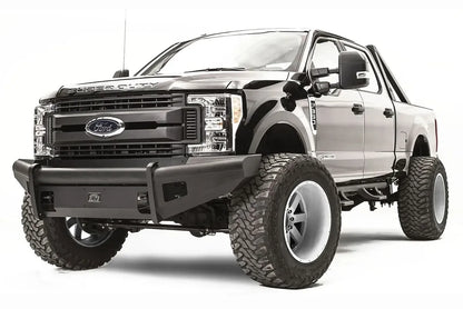 Fab Fours Black Steel Elite front bumper on a black Ford Super Duty, front driver-side three-quarter view, showing the smooth steel face, mesh-backed side openings, and the center license plate mount