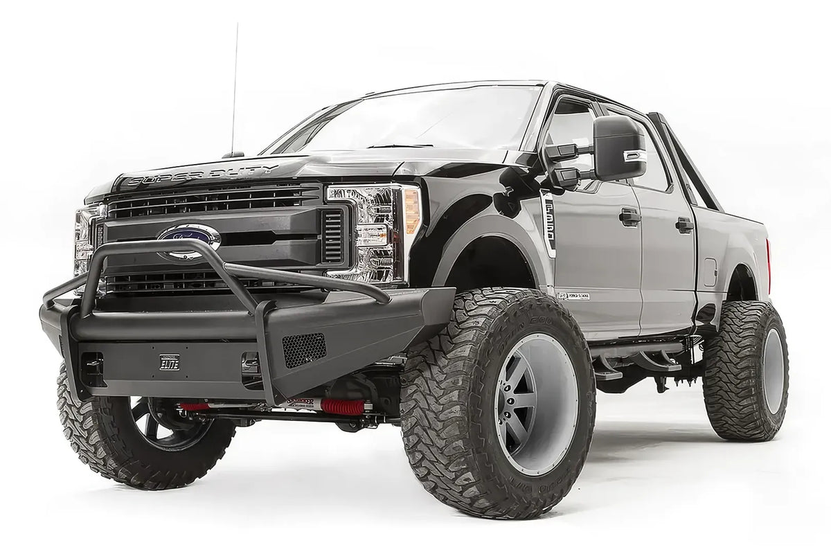 Fab Fours Black Steel Elite front bumper with pre-runner guard on a black Ford Super Duty, front driver-side three-quarter view, showing the tubular pre-runner hoop, the smooth steel face, mesh-backed side openings, and the center license plate mount