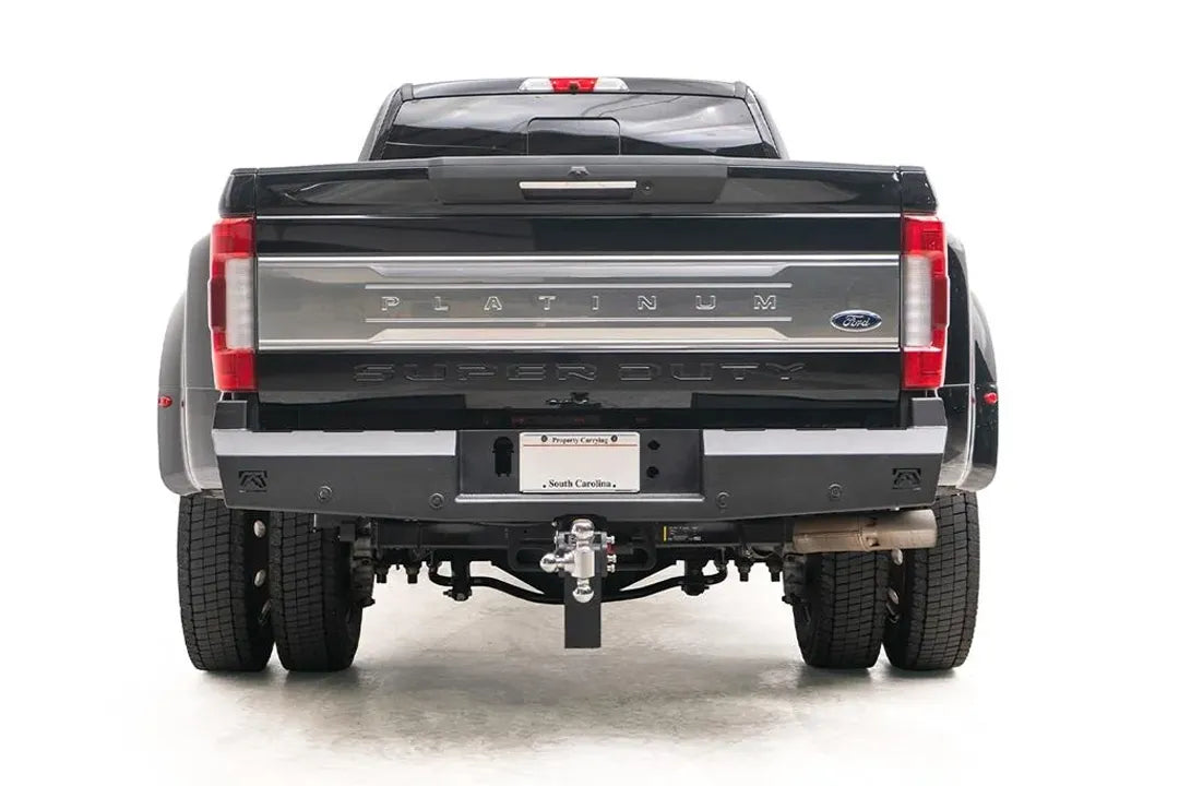Fab Fours Red Steel rear bumper on a black Ford Super Duty dually, rear view showing the matte black bumper, center license plate mount, Fab Fours logo cutouts and retained receiver hitch