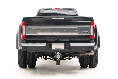 Fab Fours Red Steel rear bumper on a black Ford Super Duty dually, rear view showing the matte black bumper, center license plate mount, Fab Fours logo cutouts and retained receiver hitch