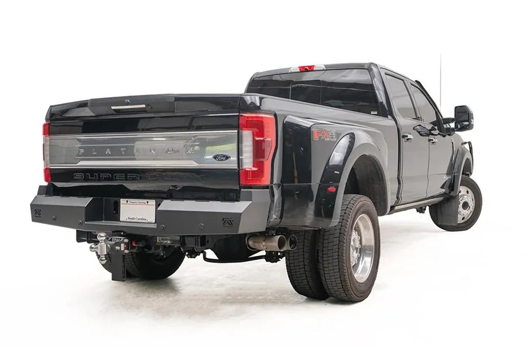 Fab Fours Red Steel rear bumper on a black Ford Super Duty Platinum dually, rear passenger-side view showing the bumper's formed steel ends and logo cutouts