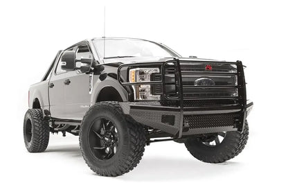 Fab Fours Black Steel front bumper with full guard on a black Ford Super Duty, front passenger-side three-quarter view, showing full grille guard with mesh insert, diamond-plate face panels, the center license plate mount, and angled side wings