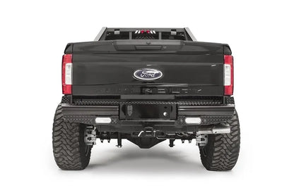 Fab Fours Black Steel rear bumper on a black Ford Super Duty, straight-on rear view, showing diamond-plate top surfaces, integrated backup light openings, and the center receiver hitch access